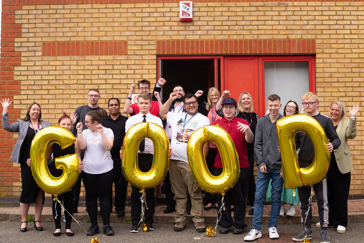 Job Coaches, staff and interns celebrating and cheering. Some interns are holding balloons which spell out good.