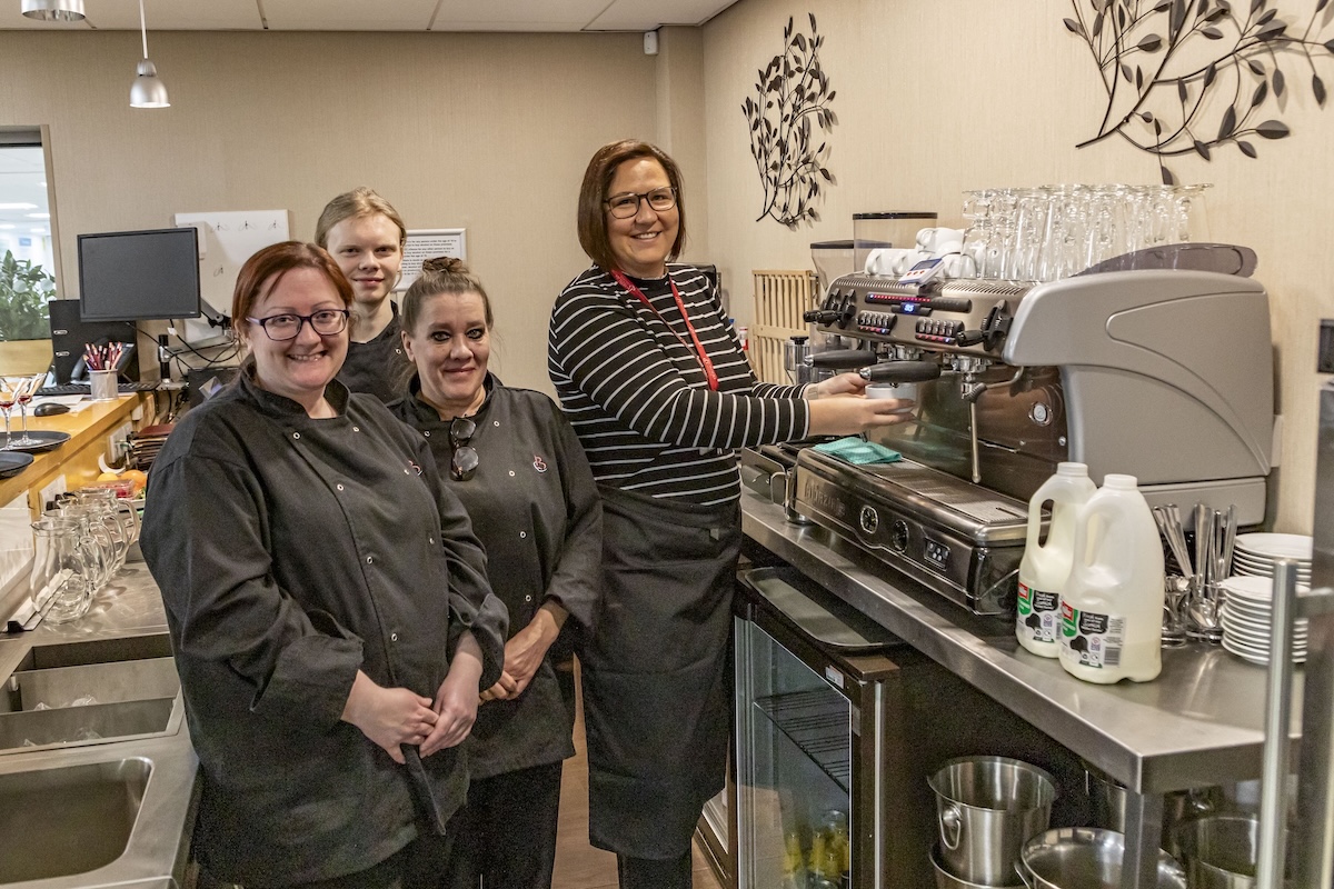 Group of catering students and staff standing in a restaurant setting next to a coffee machine
