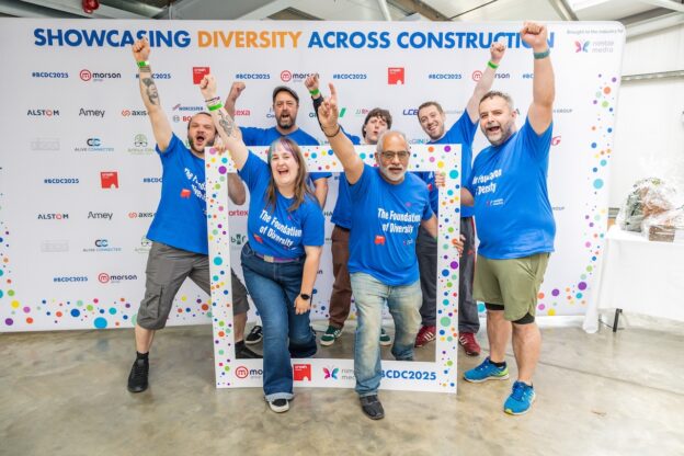 The LCB team of 7 staff pose together with fists pumped in the air, standing in front of an event backdrop, excited to start the event.