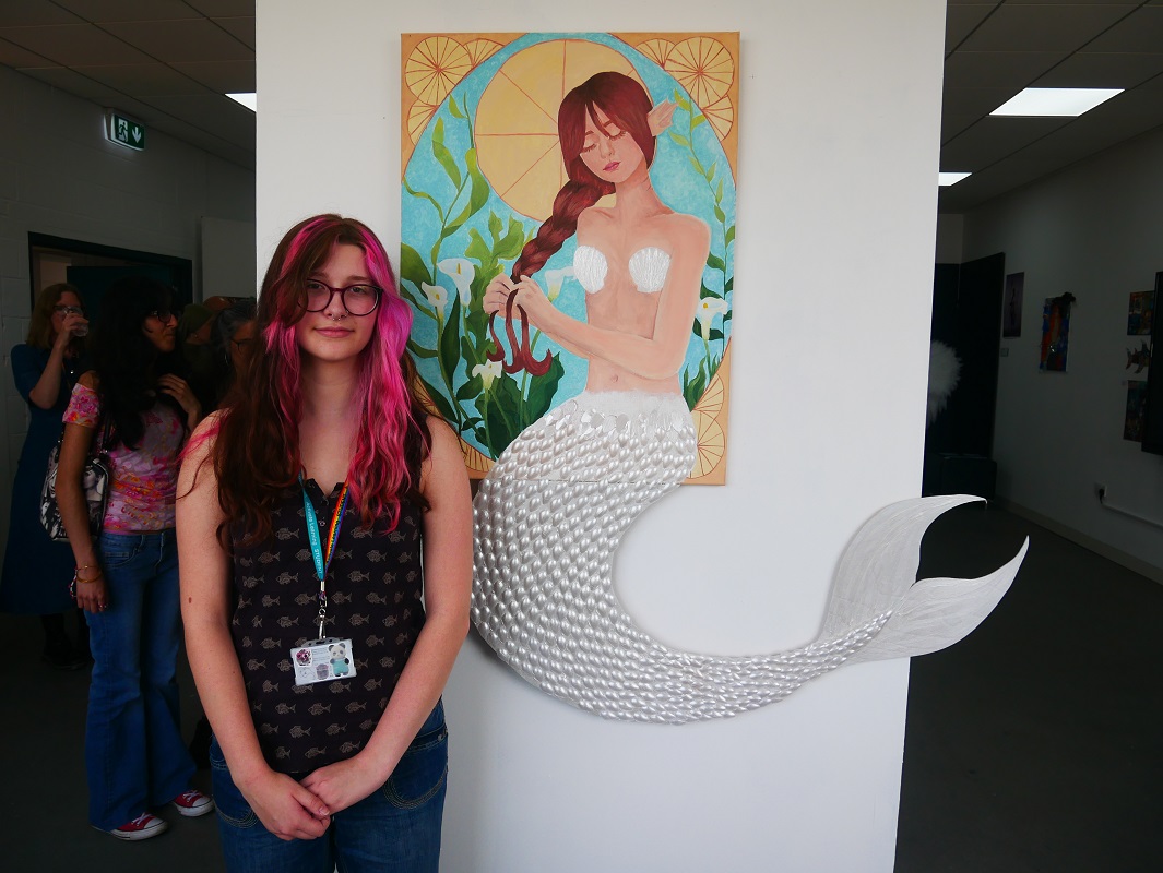 Quin Gundry, Creative Practice Art, Design and Communications Level 3 Extended Diploma, standing by her Mermaid mixed media picture.